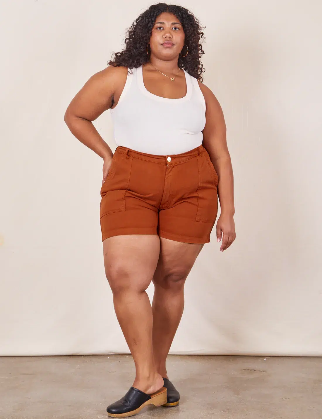 A plus size model in orange shorts and a white tank. 