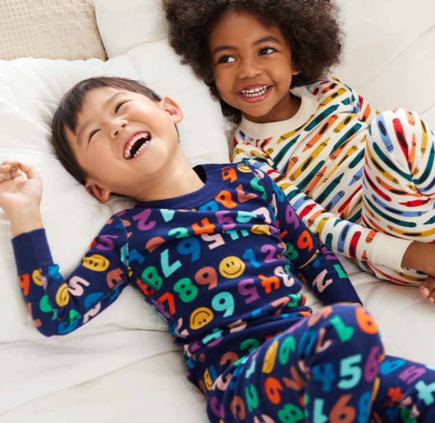 Two kids laugh and lounge in their pajamas.
