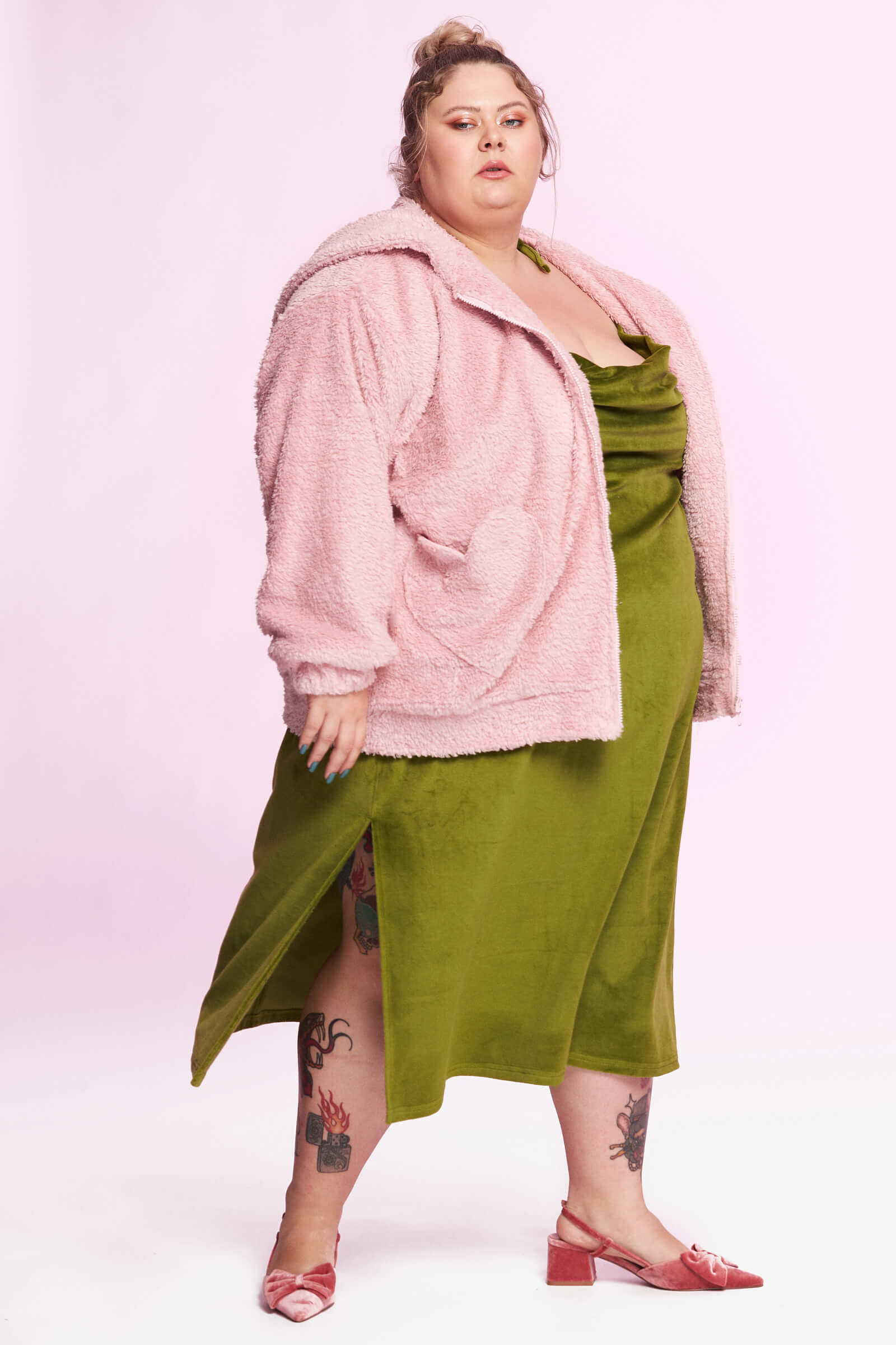 A plus size model in an acid green silk dress with pink fuzzy jacket.