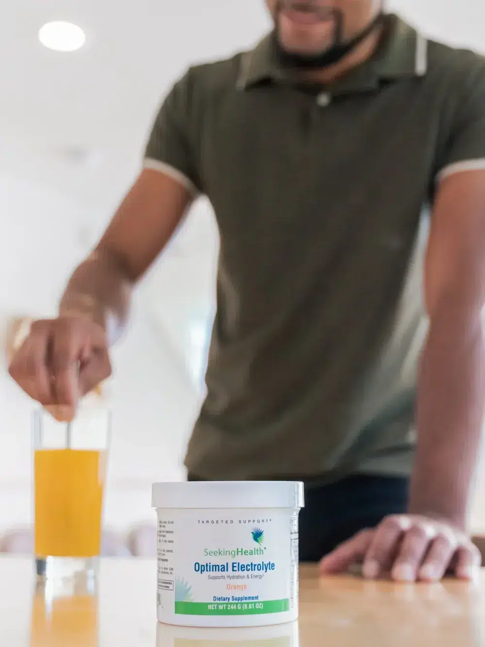 A tub of the Electrolyte product with an out-of-focus man stirring a glass in the background. 