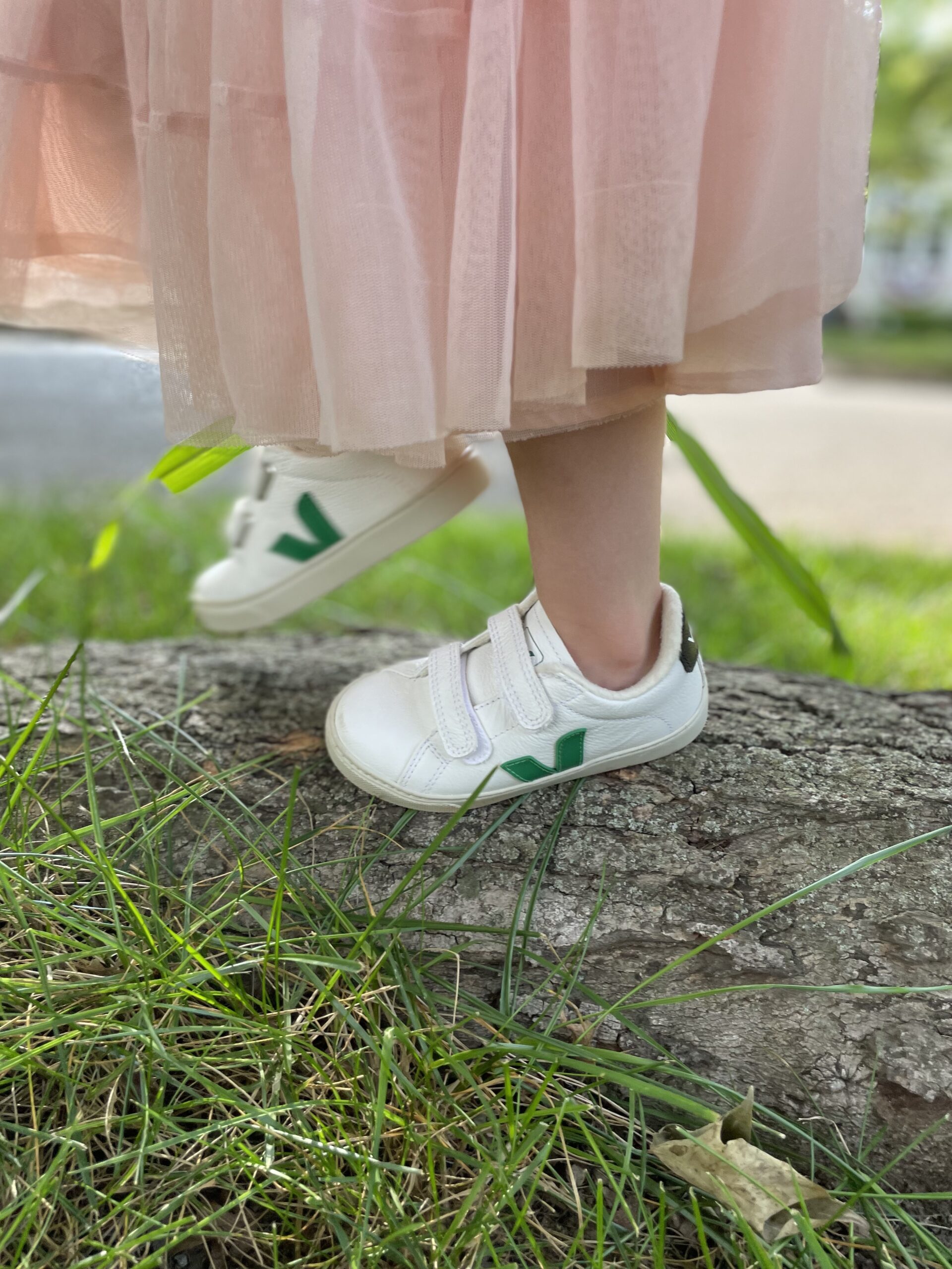 A close up of kid's feet on a log wearing Veja sneakers.