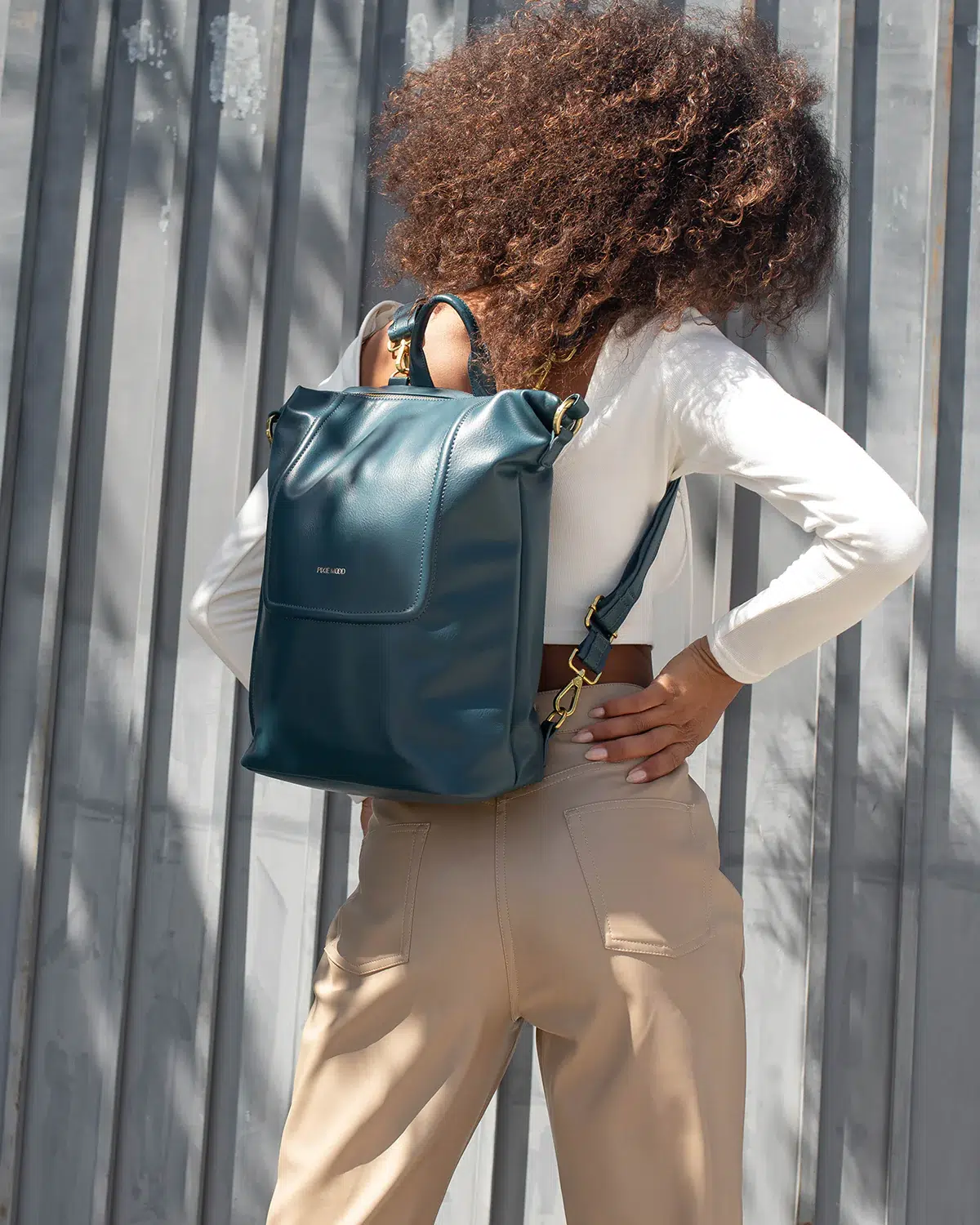 A model wears a teal leather backpack. 