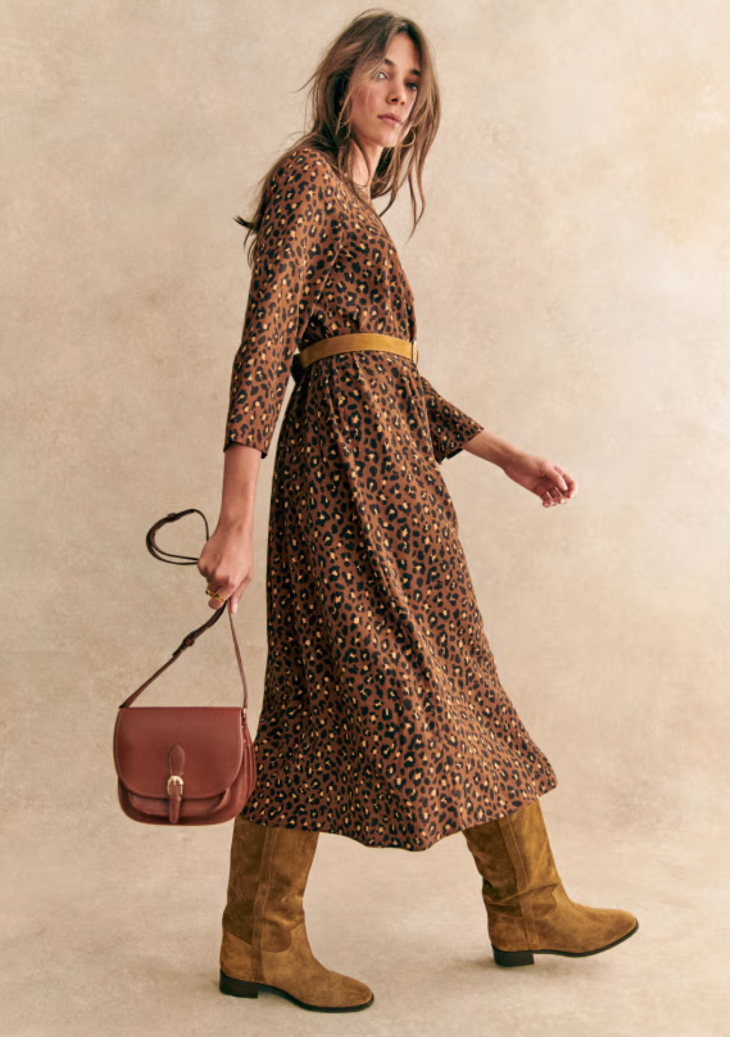 A model walks by holding a leather bag.