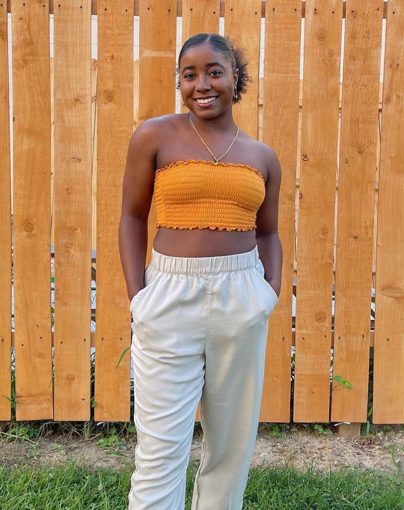 A petite woman in an orange tube top and light colored pull on pants. 