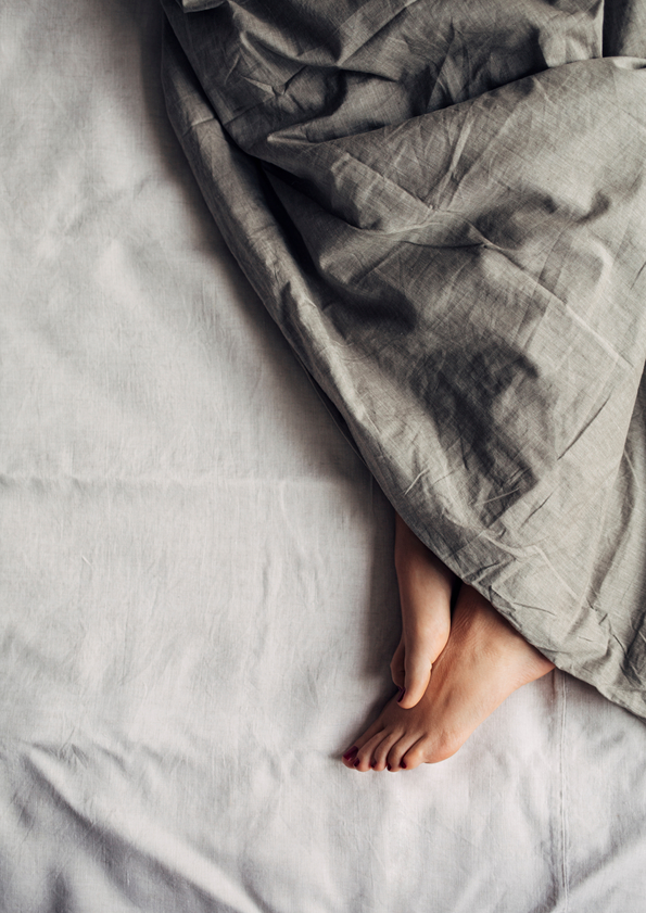 Feet of a woman sleeping under a comforter.