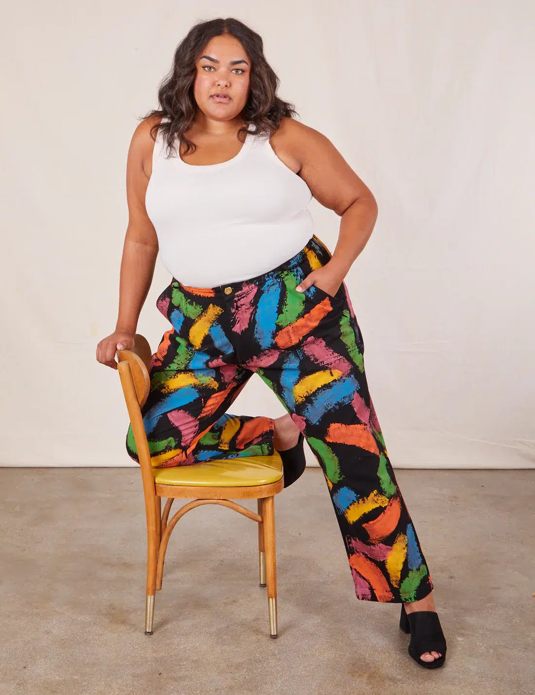 A plus size model in a white tank and black pants with colorful painted print.