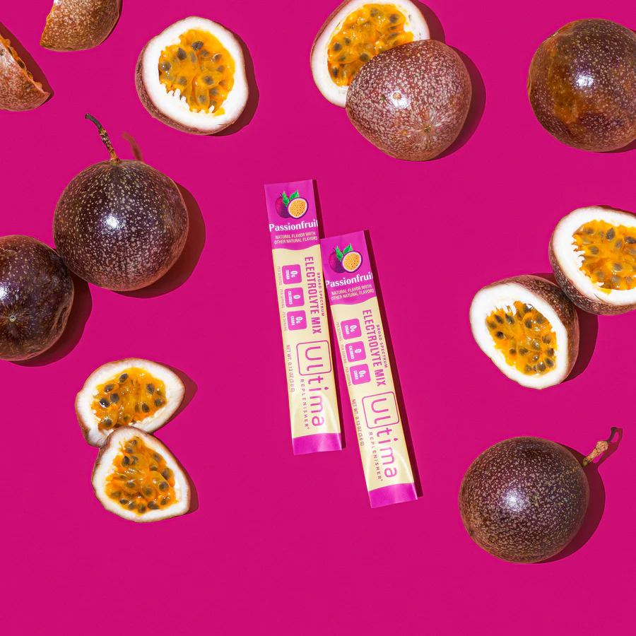 Two packets of the product on a hot pink background surrounded by sliced passionfruits.