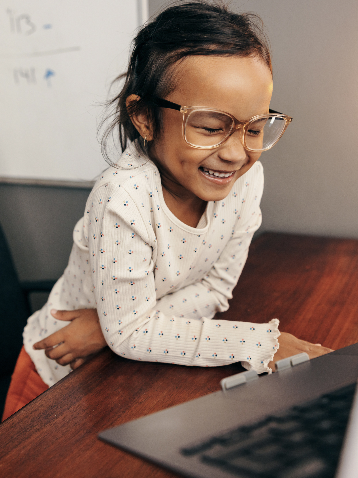 A young girl with glasses laughs in front of a computer. 