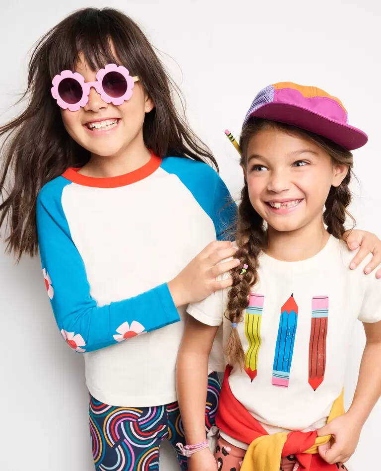 Two grade school age girls smile with their arms around each other while wearing Hanna Andersson clothes. 