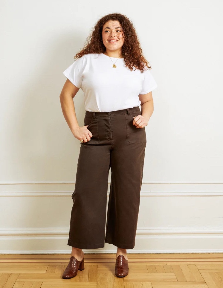 A plus size model in brown wide leg pants and a white tee.