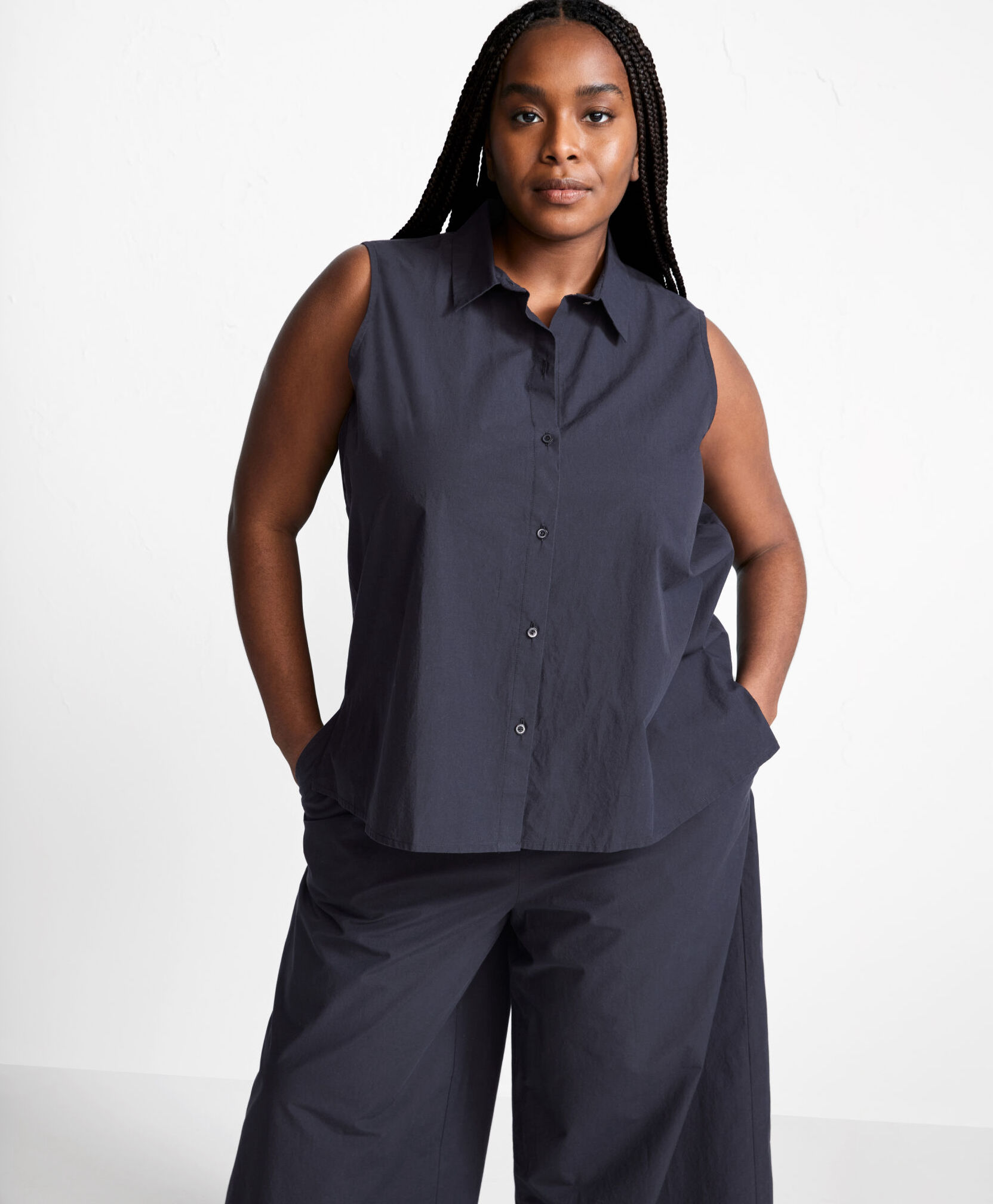 A plus size model in a sleeveless collared button down and pant set.