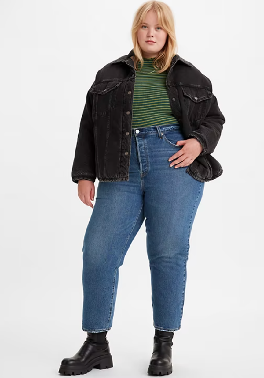 A plus size model in dark jeans and a black denim jacket.