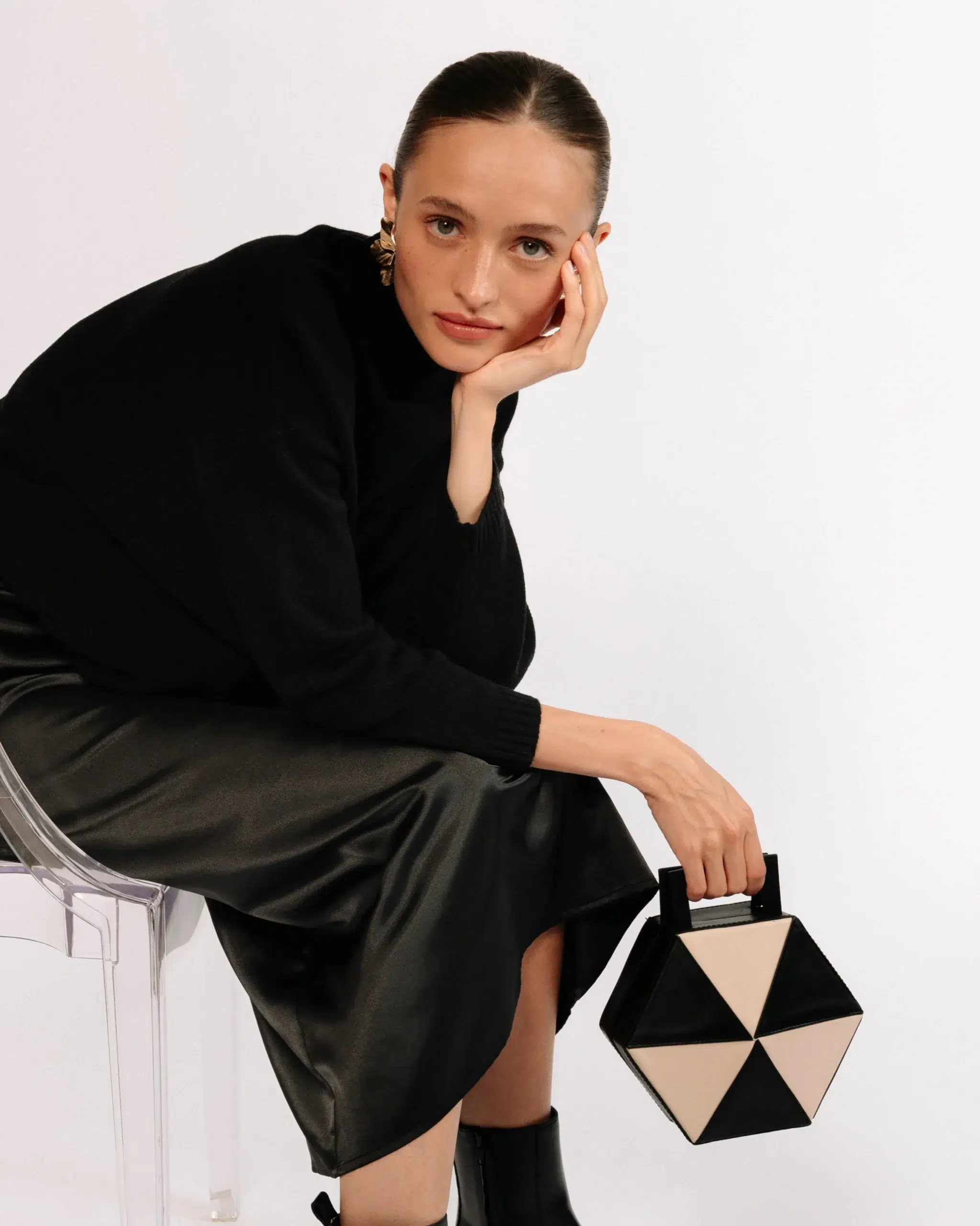A model holding a tan and black hexagonal purse. 