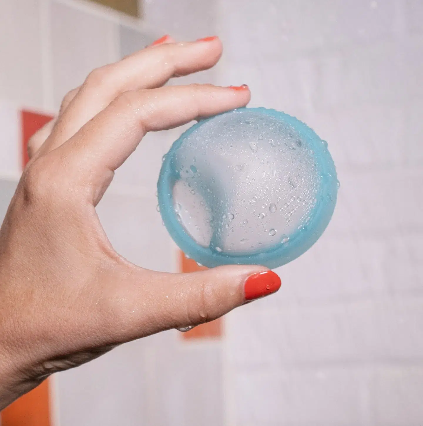 A hand holds a blue Cora menstrual disc out in a shower. 