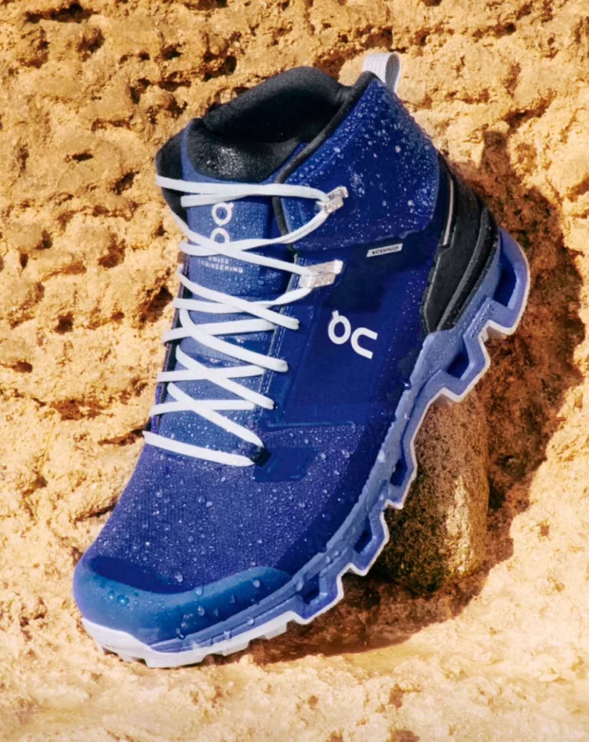 A blue On hiking boot in the sand.
