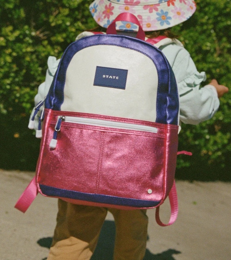 A child with a STATE backpack walks outside.
