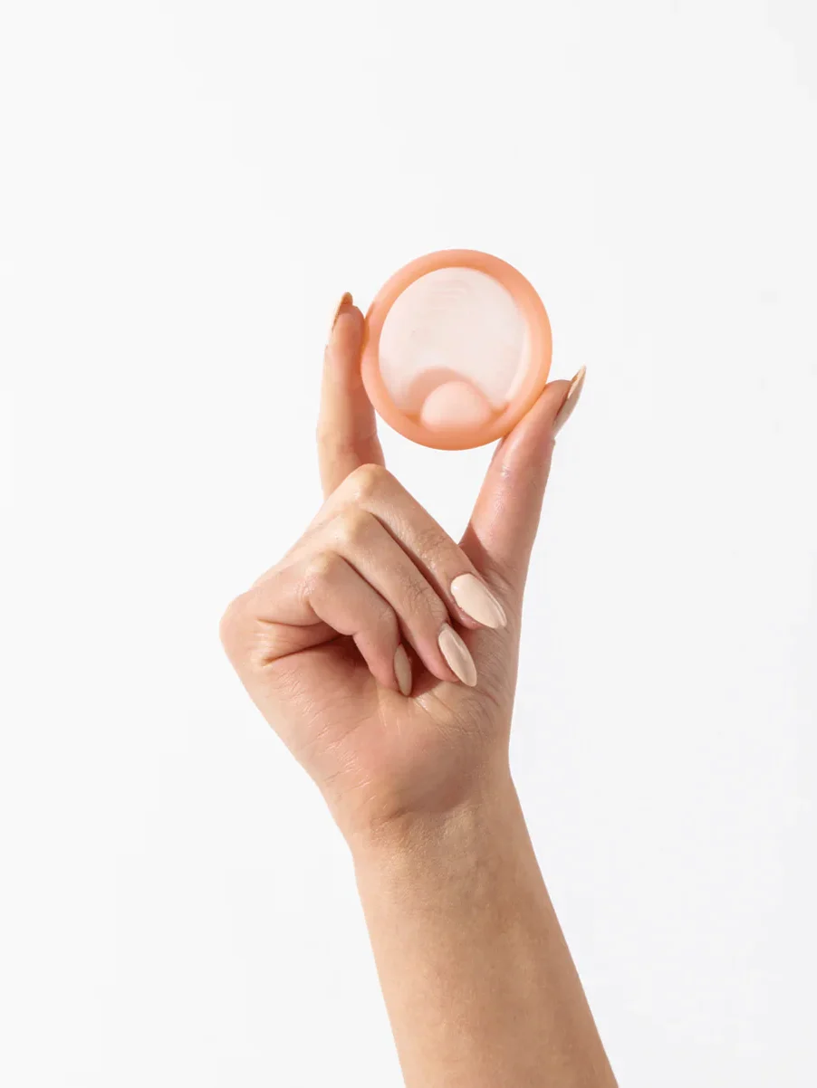 A hand holds up a pink Saalt menstrual disc