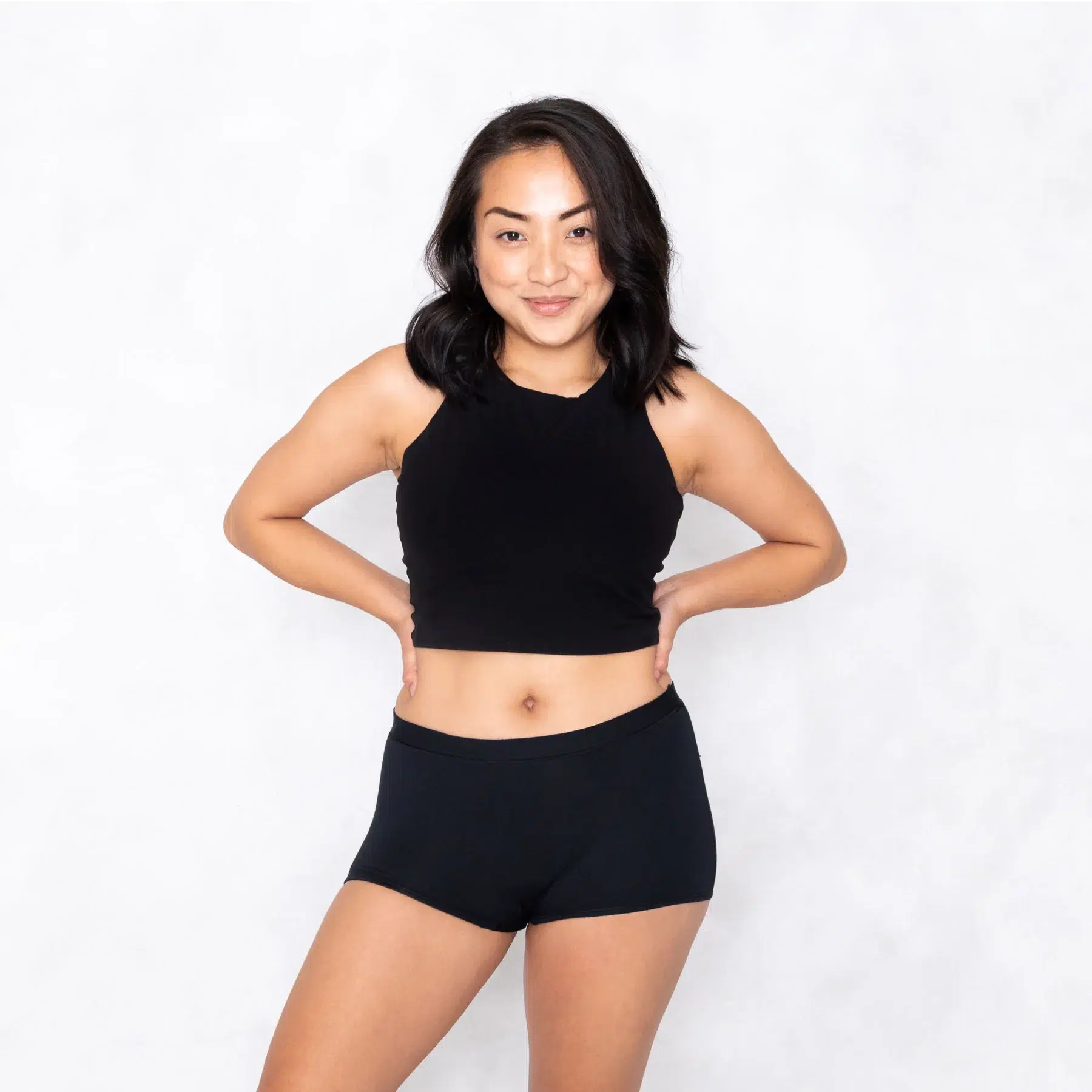 A woman in a black cropped tank and black period boyshorts. 