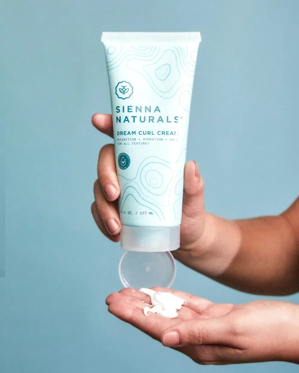 A hand squeezes a Sienna Naturals product into another hand. 