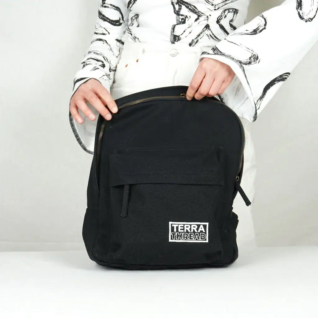 A model zips up a black Terra Thread backpack. 