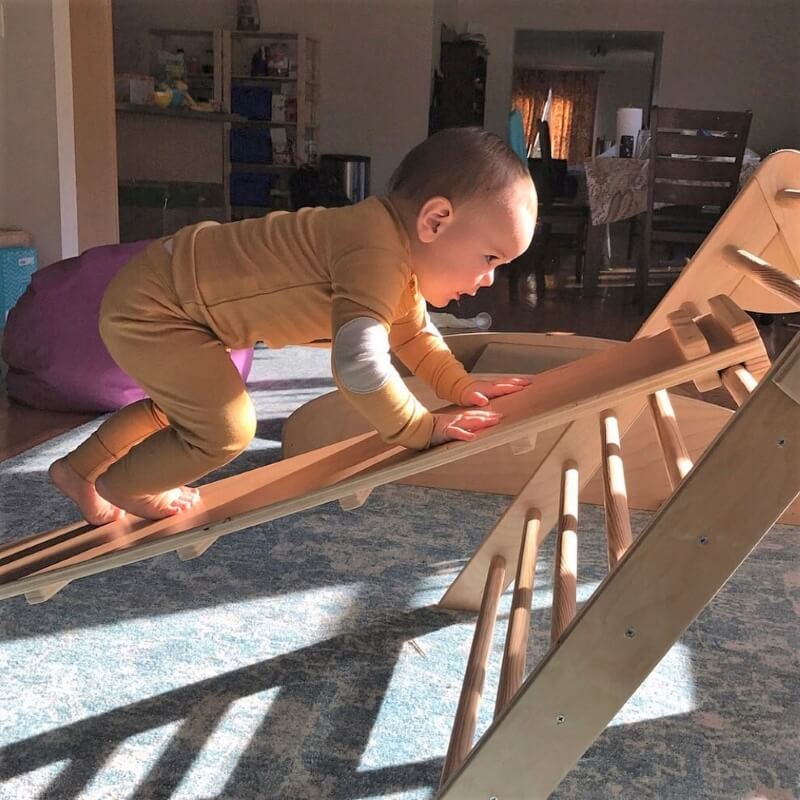 A baby climbs a ramp onto a Pikler triangle.