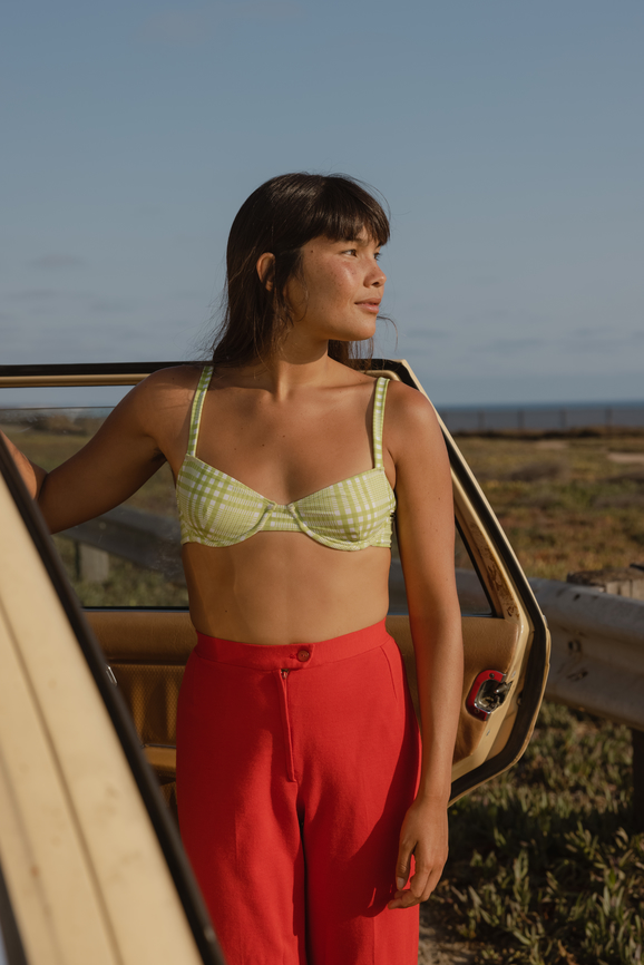 woman standing by vintage car in plaid bikini top and red pants at the coast