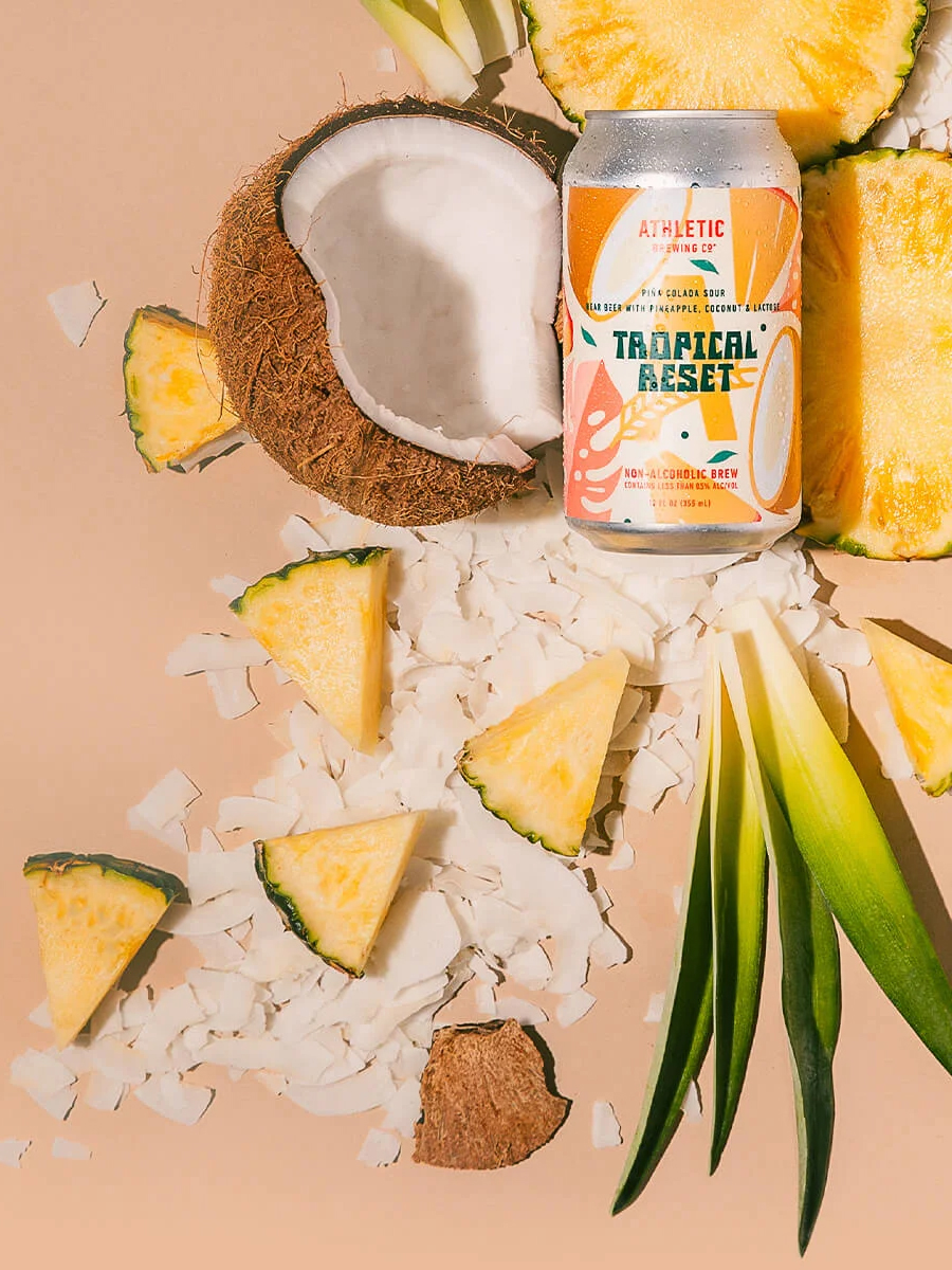 Athletic Brewing Co Tropical Reset can on a styled flat lay with a coconut and pineapple.