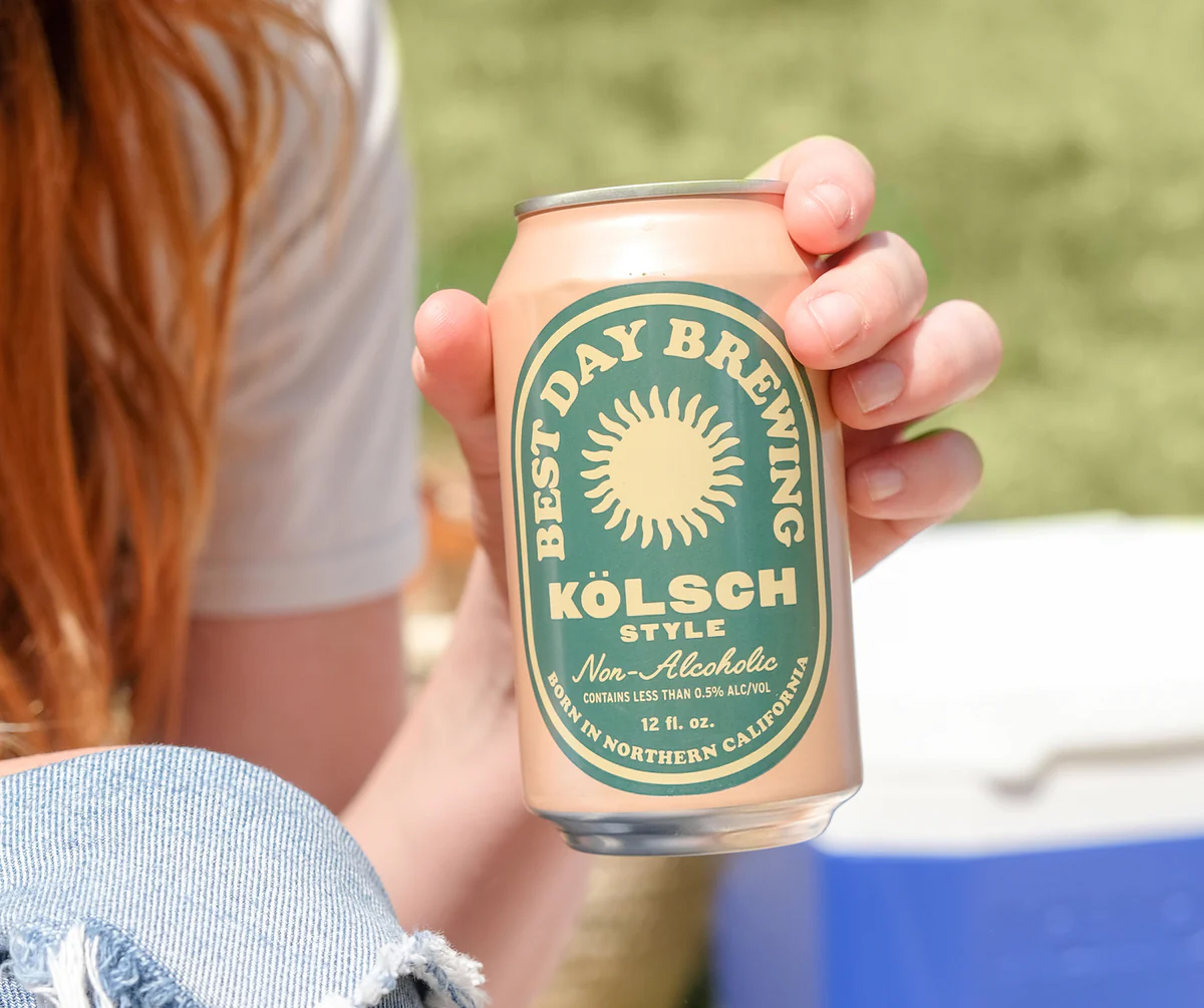 A close up of a hand holding a can of Best Day Brewing Non-Alcoholi beer. 