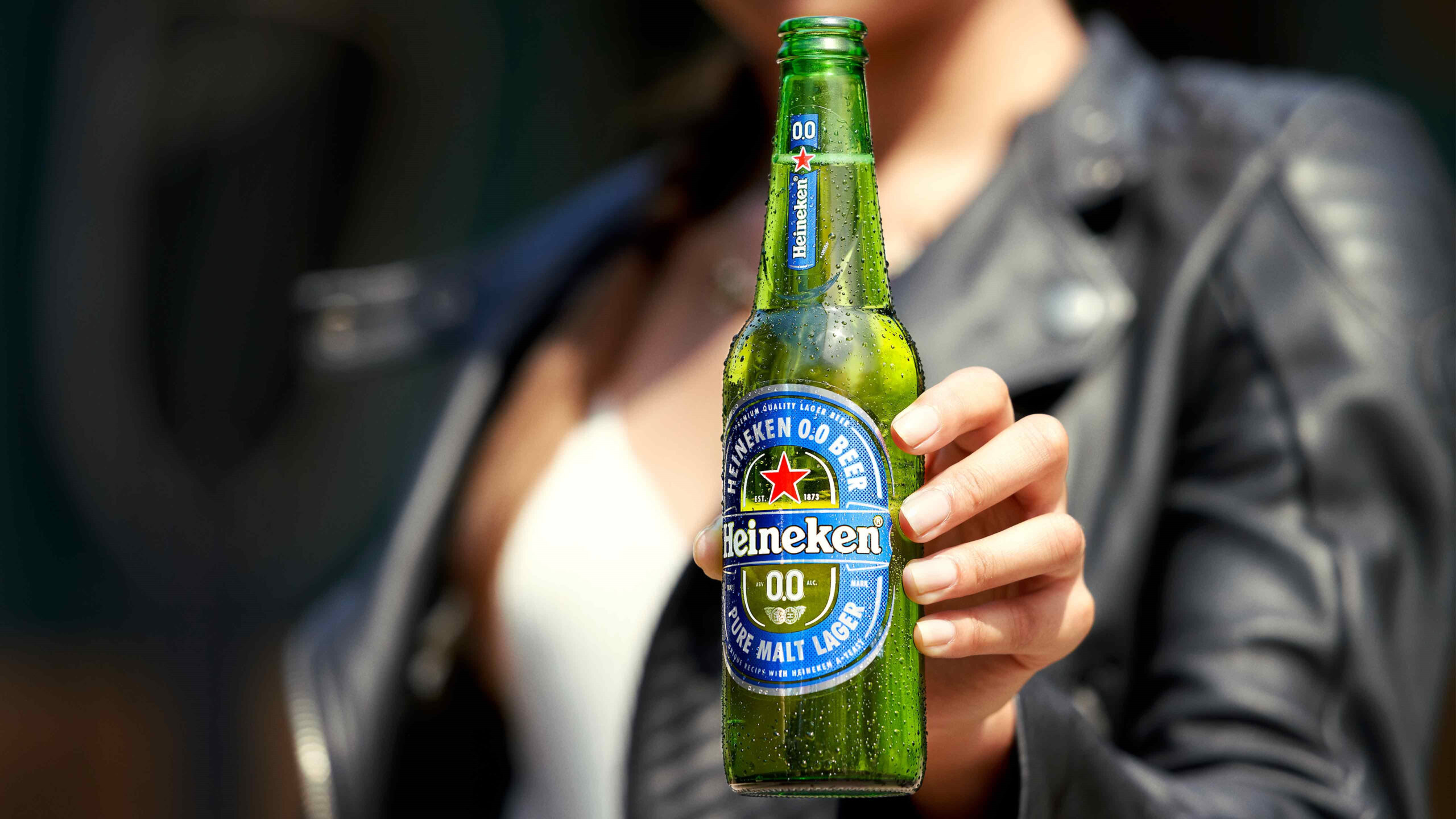 A close up of a hand holding a Heinkeen 0.0 bottle.