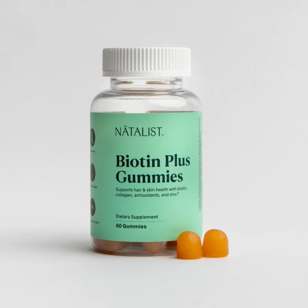 A bottle of Biotin Plus Gummies with two gummies next to it.