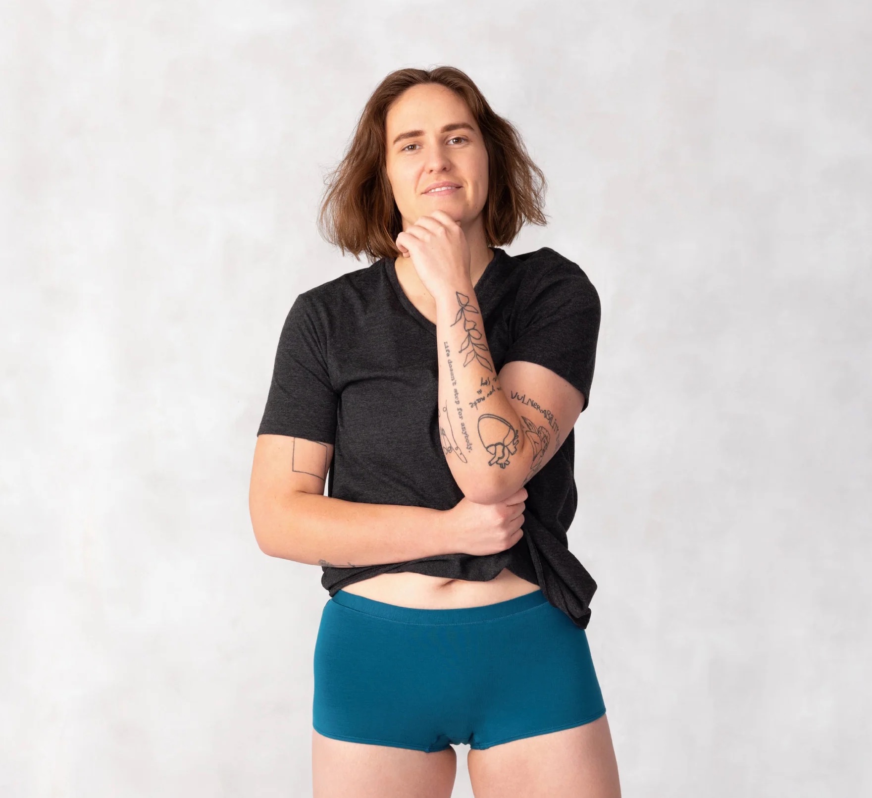 An adult in a dark gray shirt and teal period boyshorts. 