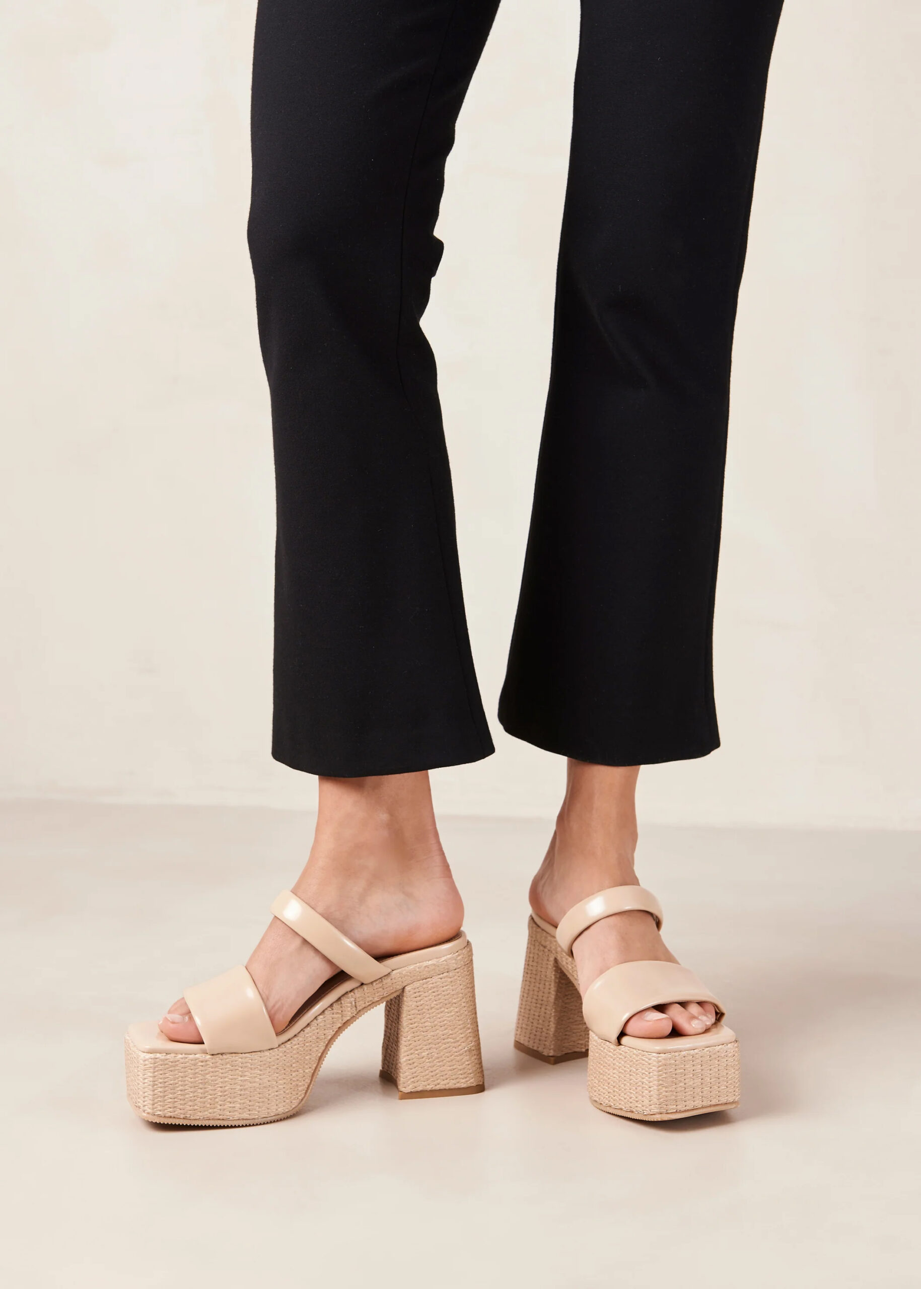 A model's legs and feet in black cropped pants and platform rattan beige-colored sandals. 
