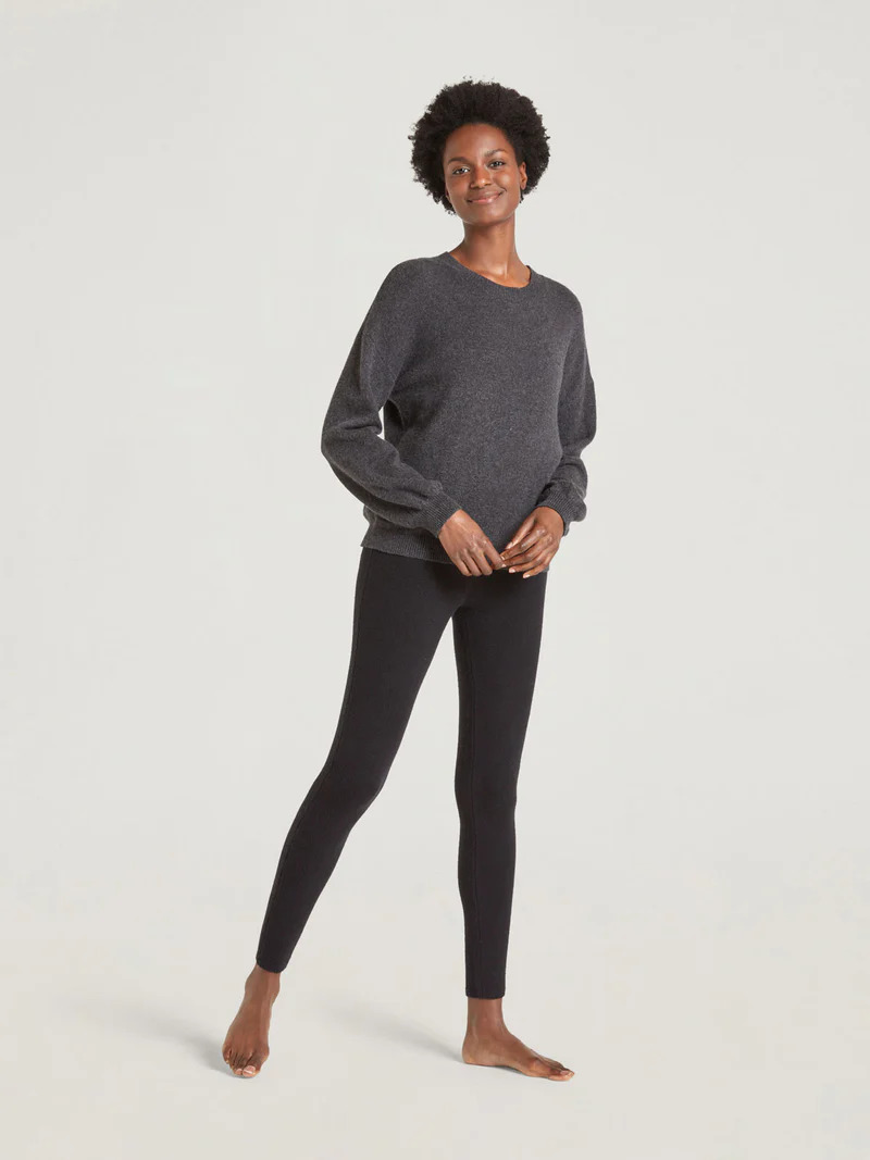 A model wearing a grey crewneck and knitted black organic cotton leggings by thought.