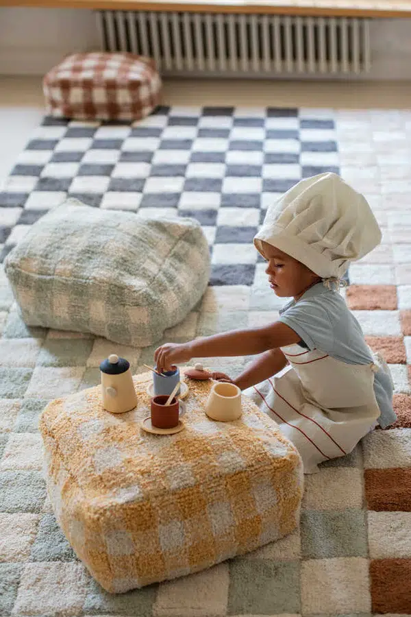 A child plays in. chef's costume on a pile of Lorena Canals' nontoxic rugs in checkerboard patterns. 