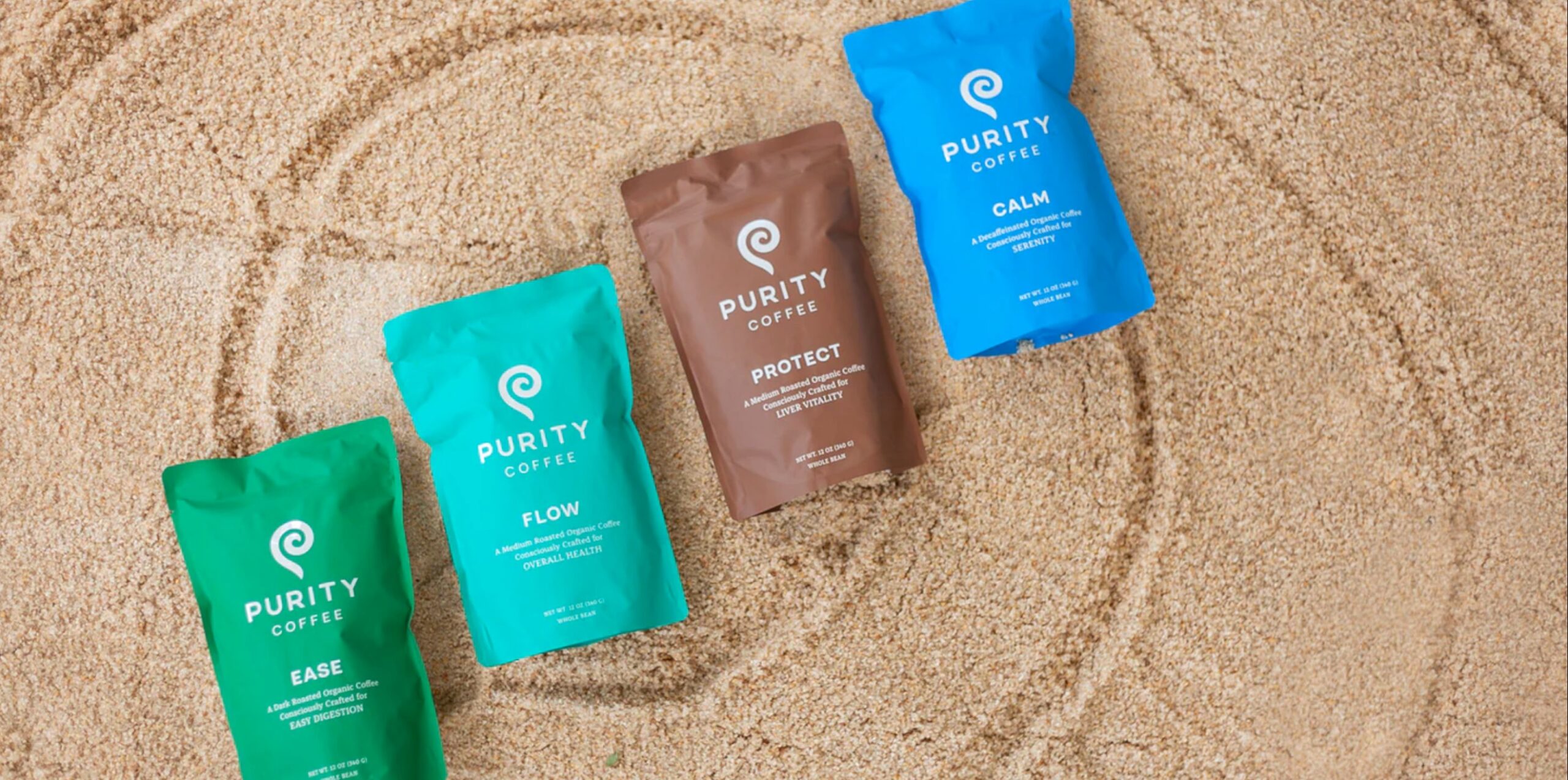 Three bags of Purity coffee lie in the sand. 