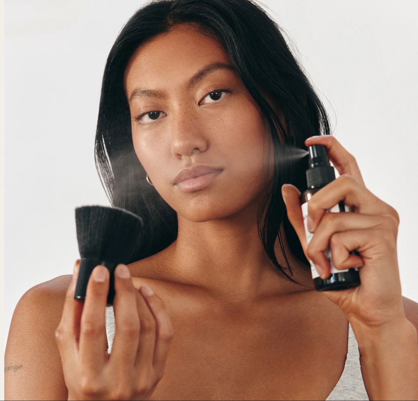A model sprays Salty Face nontoxic tanning products onto a kabuki brush.