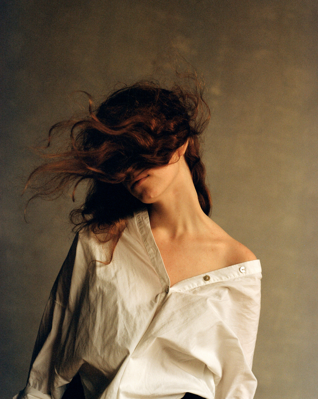 Portrait of young woman with curly red hair hiding her face wearing white shirt