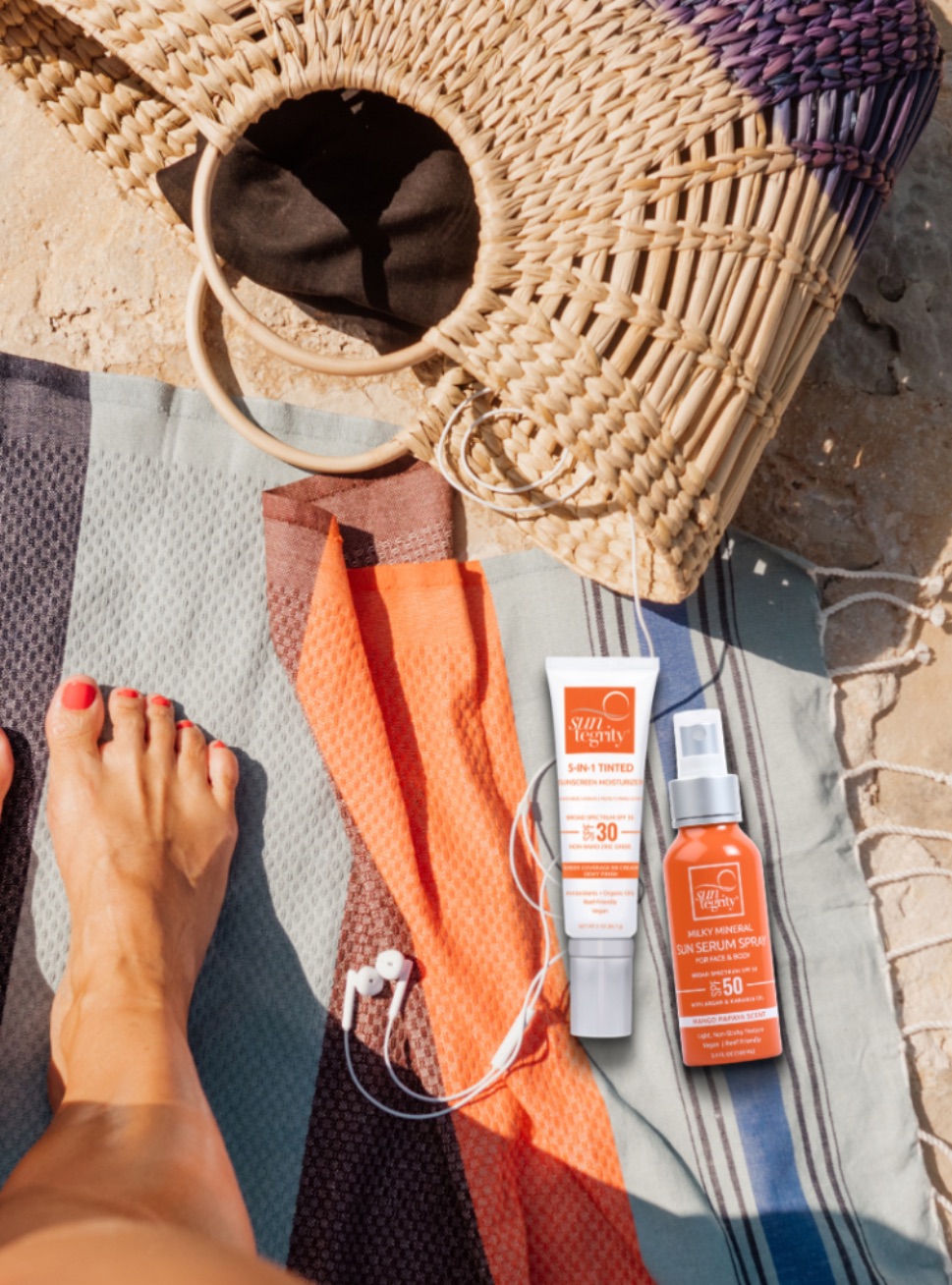 A model's foot on a beach with Suntegrity nontoxic self-tanner products lying on the towel. 