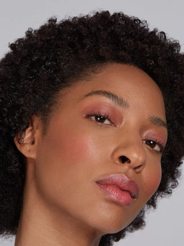 A close up headshot of a woman with short black curly hair wearing Axiology's multi-use balm.