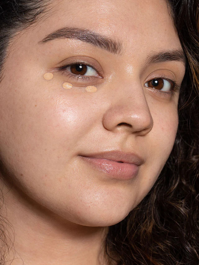 Closeup of a woman's face with Ilia's skin tint foundation dotted under one of her eyes.