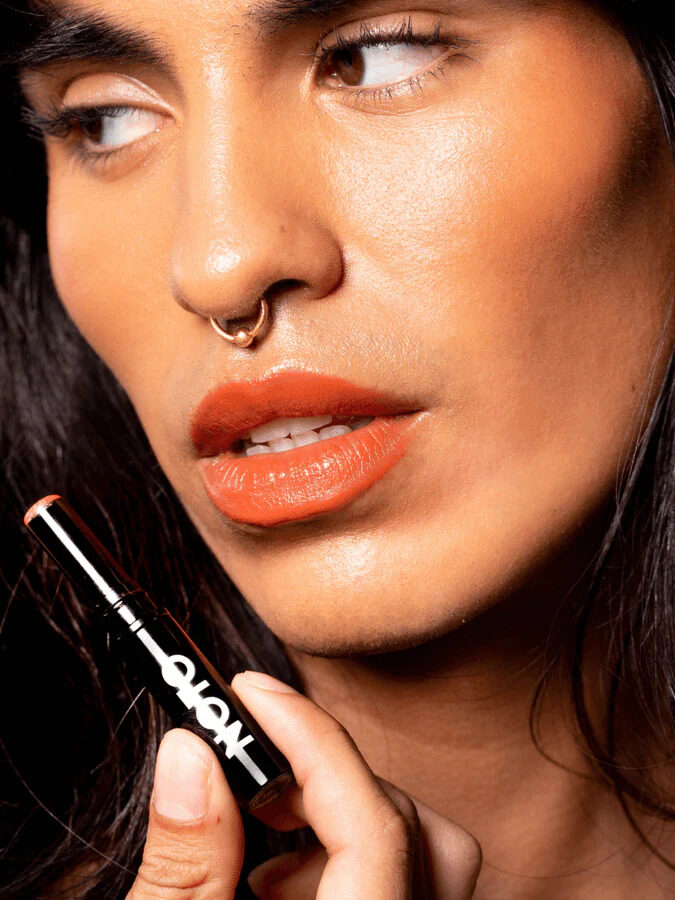 A closeup headshot of a woman with dark hair wearing Noto's multi-use stick on her lips and holding the product up.