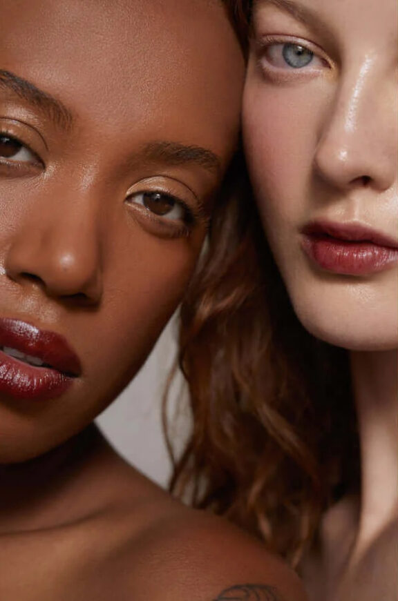 Close up headshot of two women leaning into eachother wearing Noto multi-use-makeup sticks in a dark red shade.