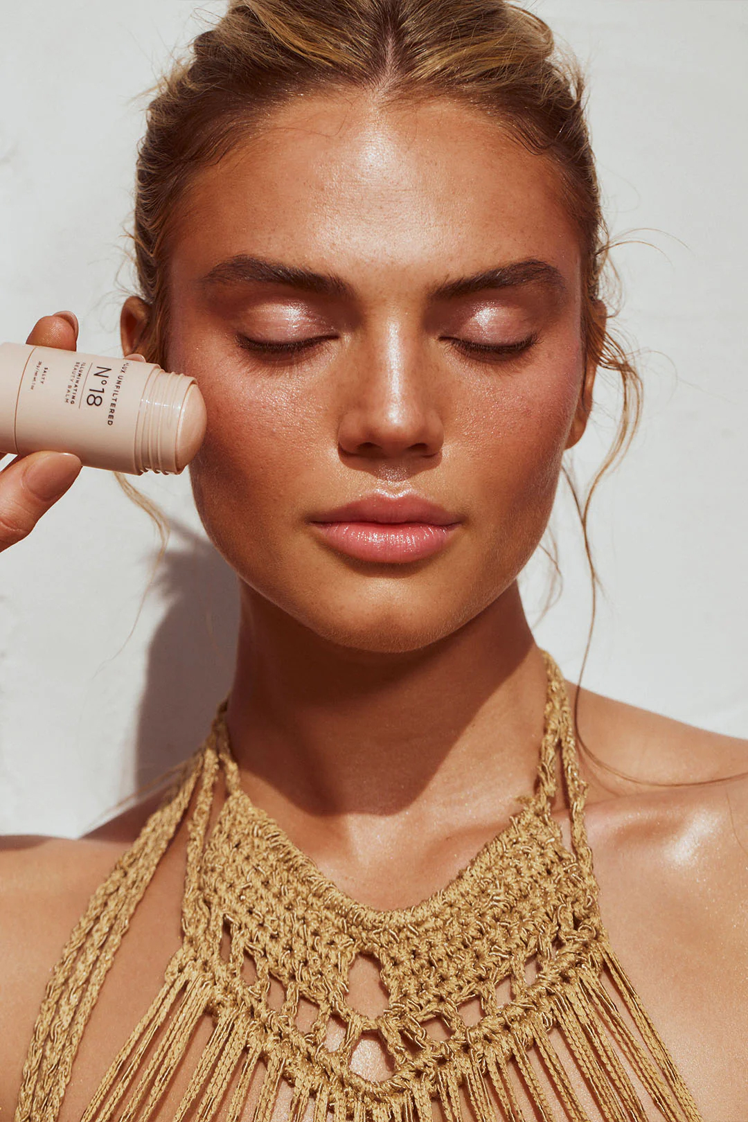 A model holds a Lux Unfiltered illuminating stick to her cheek.