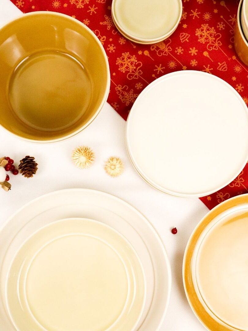 Overhead shot of various colorful Tripware ceramic plates and bowls arranged next to each other on a white table with a red runner.