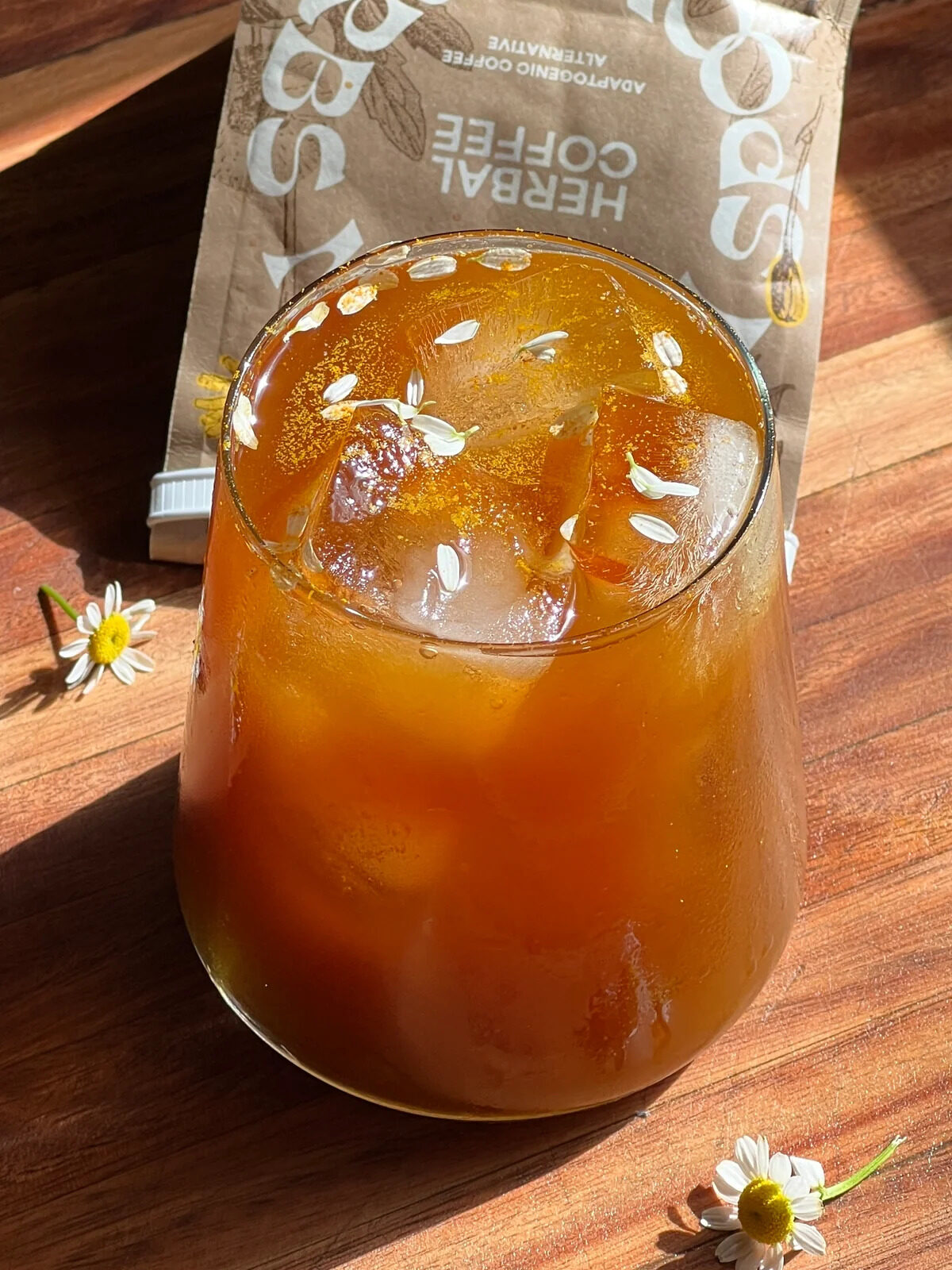 A glass cup filled with iced Wooden Spoon Herbs coffee alternative, topped with flower petals.