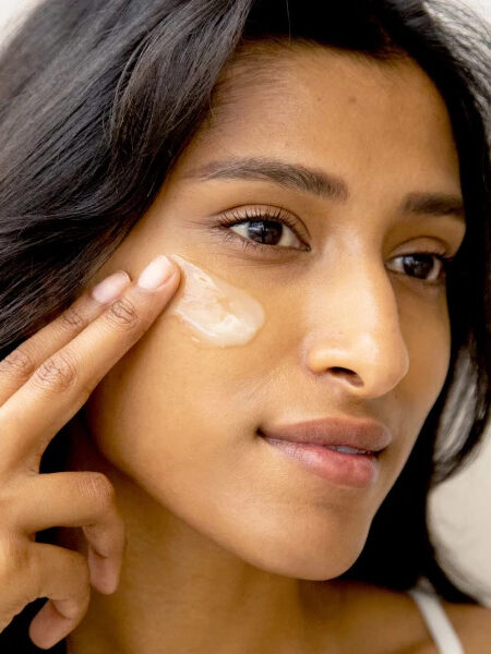 A closeup of a woman applying 100% pure skincare to her cheek.