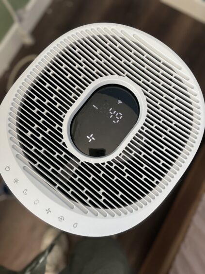 Top view of a white air purifier with digital display showing numbers and various touch control icons along the edge.