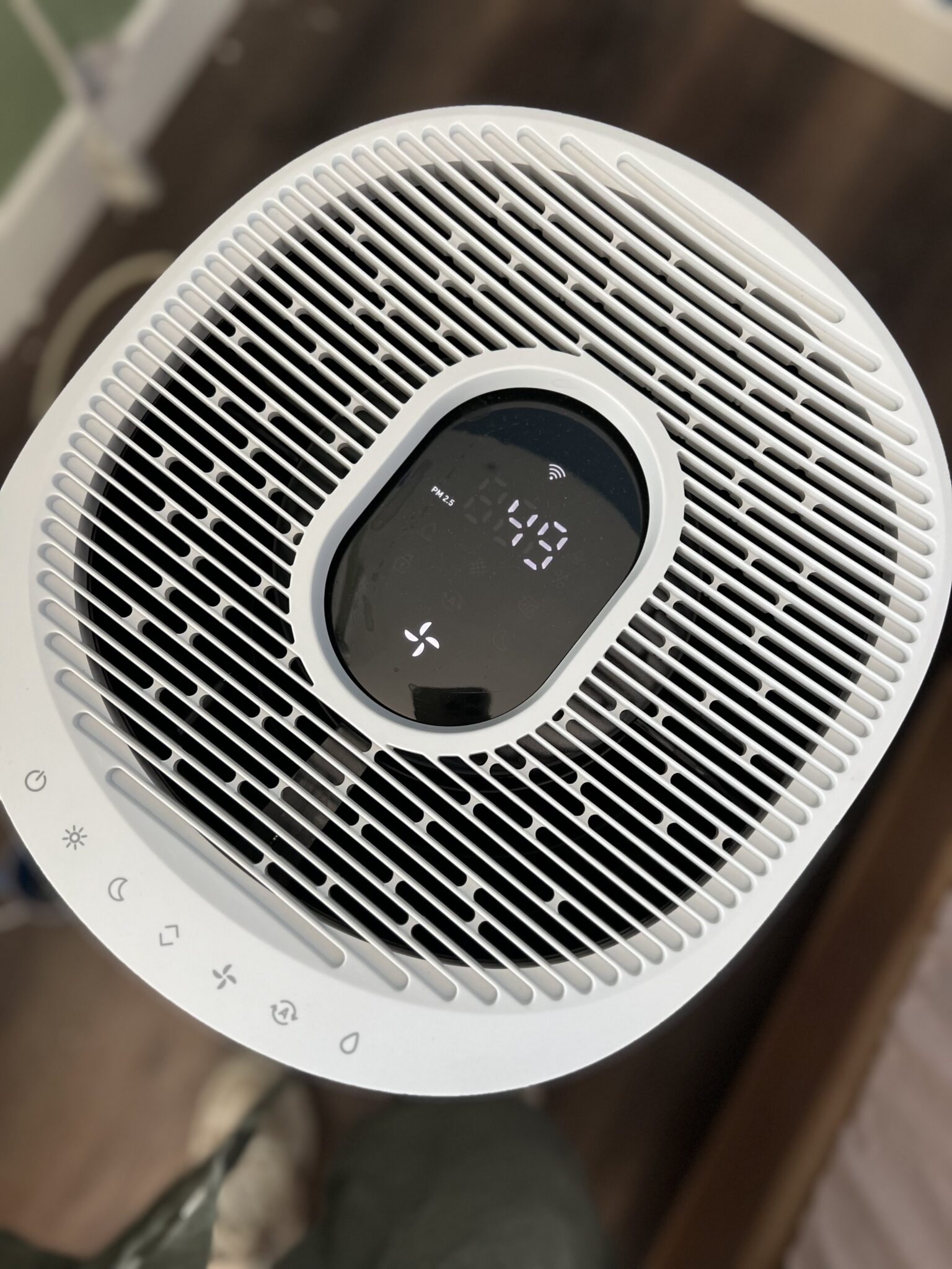 Top view of a white air purifier with digital display showing numbers and various touch control icons along the edge.