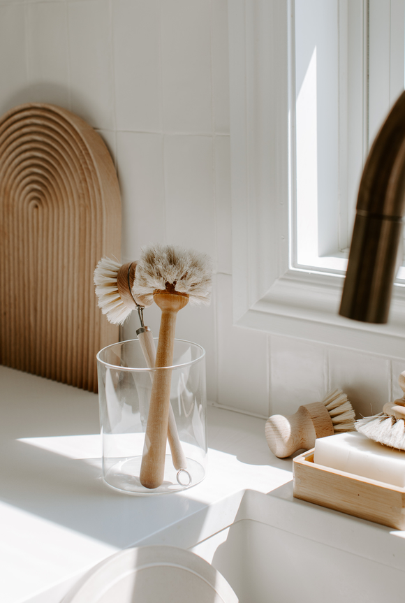 Eco-friendly wooden dish brushes in a glass container, set on a kitchen countertop.