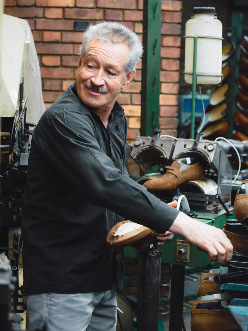 An artisan looking back while using a machine to craft Beckett Simonon shoes.